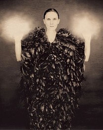 portrait of woman wearing a black feathered garment with glowing hands upraised